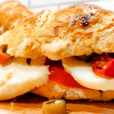 A front view of a sliced gluten free baguette filled with mozzarella, tomatoes and peppers, with 2 more sitting in the background
