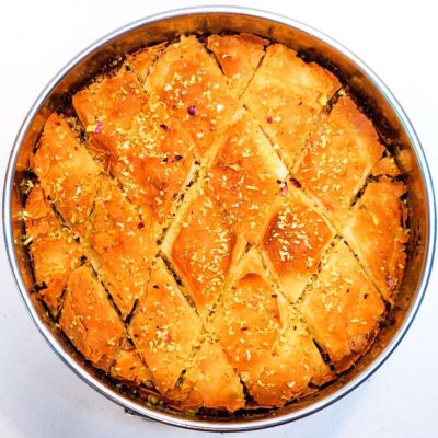 The top down view of a crisp and flavorful baklava, that is still in the cake tin and topped with shaved pistachio