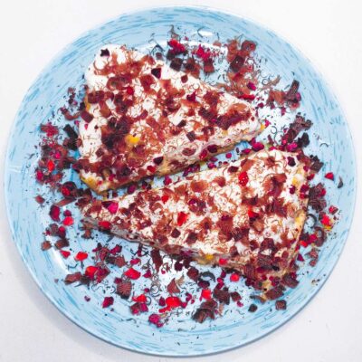 A top down view of a gluten free banoffee pie, served on a blue plate and topped with shaved chocolate and dried strawberries