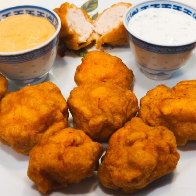 A front view of 8 fried chicken nuggets, one sliced in half, served with 2 sauces