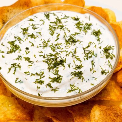 An upper front view of some homemade chips, served with a bowl of yogurt and dill sauce