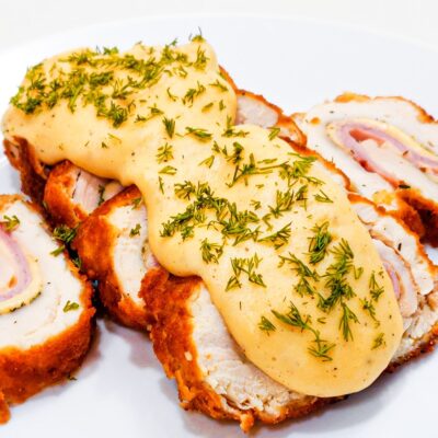 A side front view of a chicken cordon bleu, served with a mustard sauce and topped with parsley