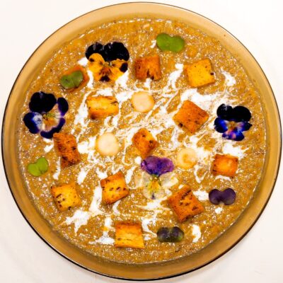 A top down view of a creamy mushroom soup, topped with gluten free croutons and edible flowers