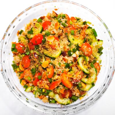A top down view of a quinoa salad, served with chopped cherry tomatoes, spring onions, cucumbers and fried almonds
