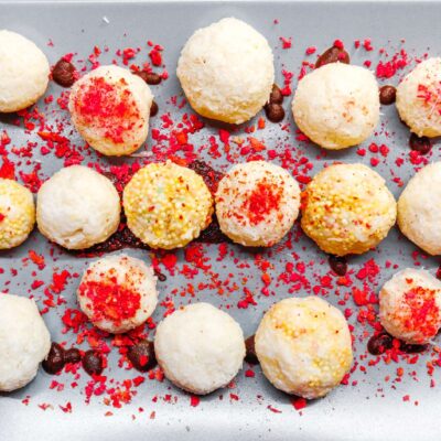 A top down view of multiple gluten free raffaello balls, on a grey plate, surrounded by dried raspberries