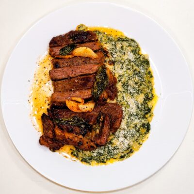 A top down view of a rib eye steak with creamy spinach, served on a plate