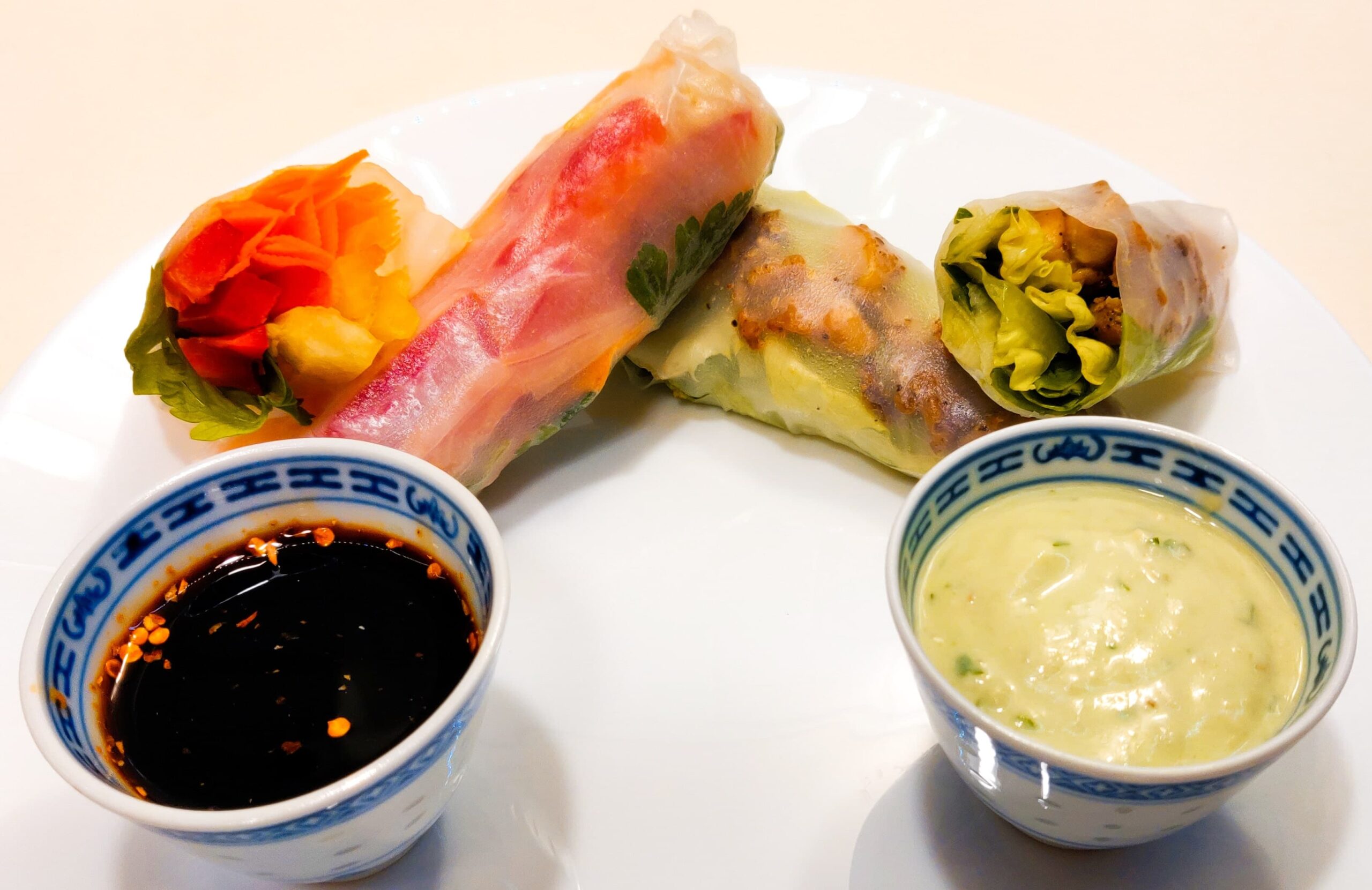 A front view of a 2 chicken spring rolls and 2 vegetable spring rolls, served with a soy sauce and an avocado sauce