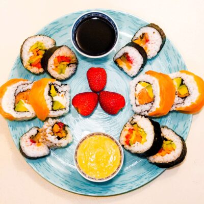 A top down view of 3 types of sushi, served on a plate with soy sauce and an avocado sauce