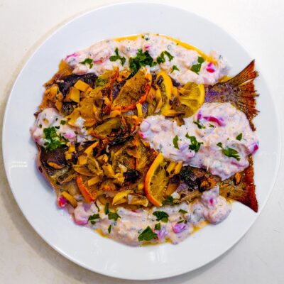 A top down view of a baked trout recipe, served with a yogurt sauce and served on a plate